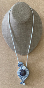 A glass and genuine leather necklace with a geometric-patterned pendant, displayed on a mannequin.