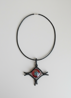 A black leather necklace with a glass pendant in the shape of an eye, featuring multicolored patterns within the eye, displayed on a wooden surface.