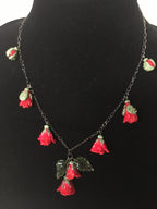 A glass necklace with red and green floral pendants displayed on a mannequin bust.