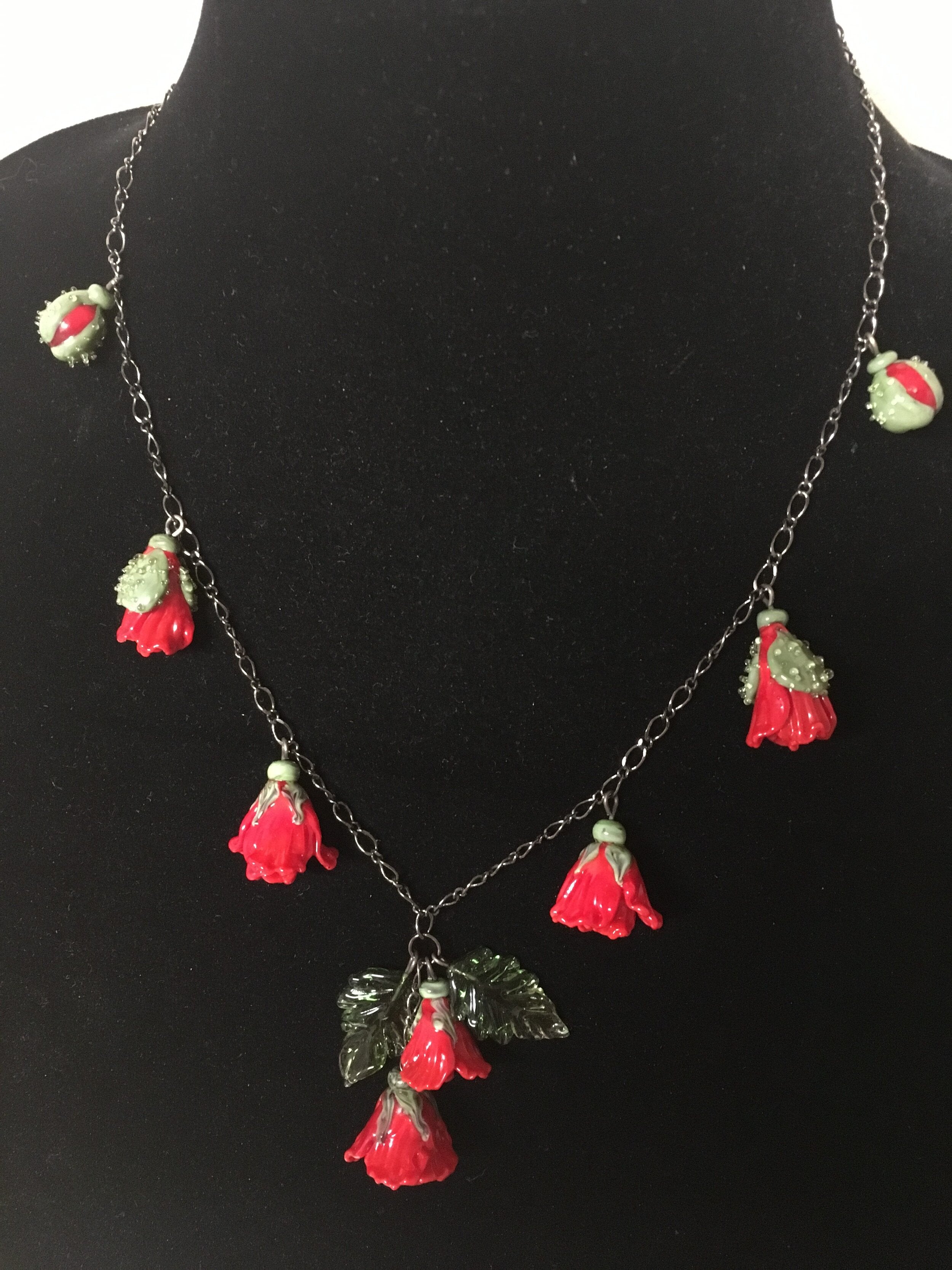 A glass necklace with red and green floral pendants displayed on a mannequin bust.